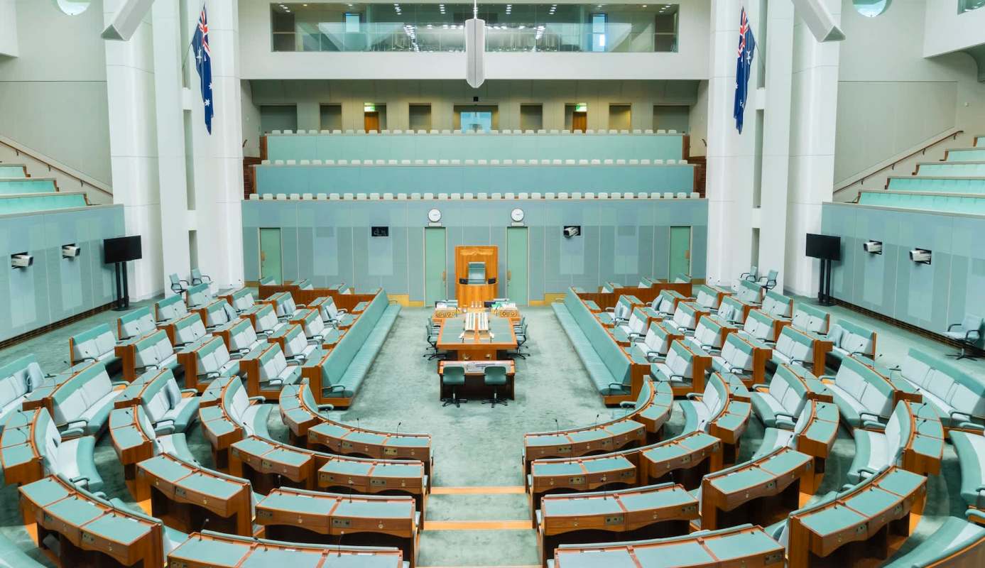 A panoramic view of an empty parliamentary chamber with green seating and wooden accents.