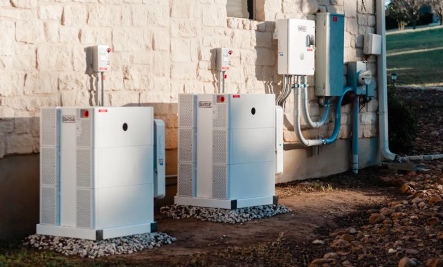 Two white utility boxes installed against a stone wall, featuring electrical components and connected pipes.