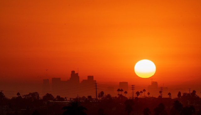 A vibrant sunset casts orange hues over a silhouetted city skyline.