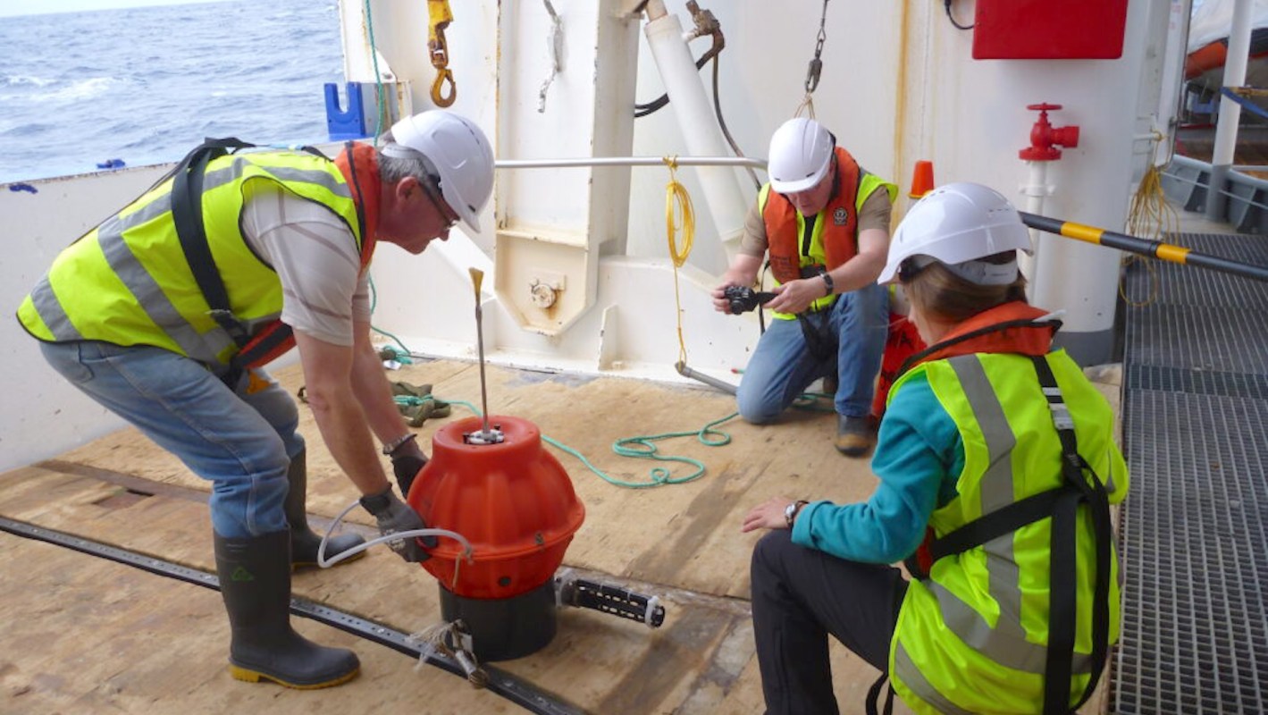 Scientists on a research vessel preparing to deploy an orange robot.
