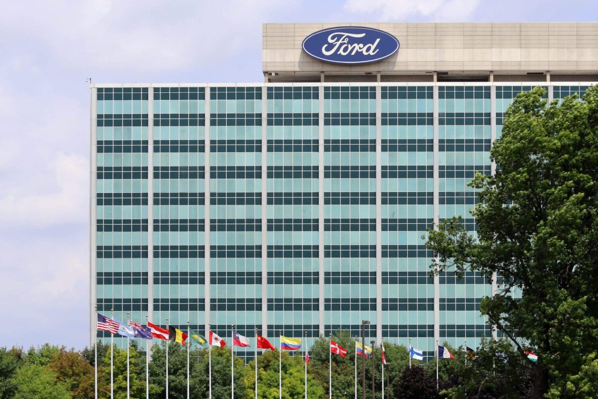The Ford headquarters is seen behind multiple international flags and greenery under a partly cloudy sky.
