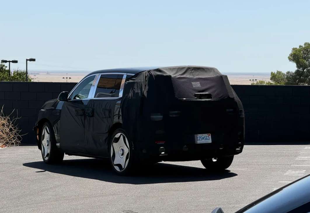 A blacked-out test vehicle is parked in a lot, partially obscured by covers and surrounded by sparse vegetation.