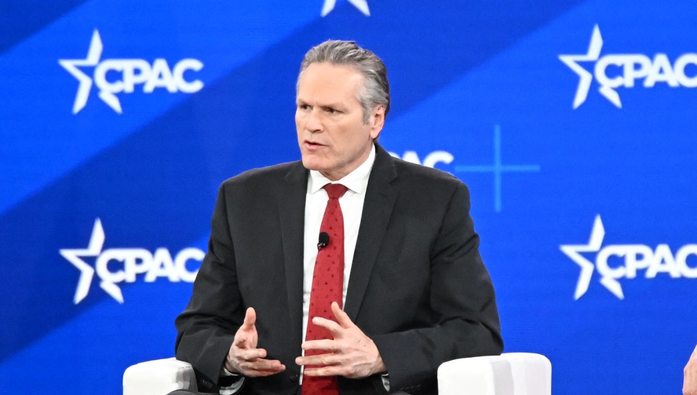 Alaska Governor Mike Dunleavy, in a suit, gestures while discussing a topic at a CPAC event.