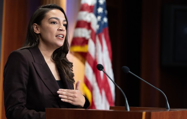 U.S. Rep. Alexandria Ocasio-Cortez speaks at a podium near an American flag.