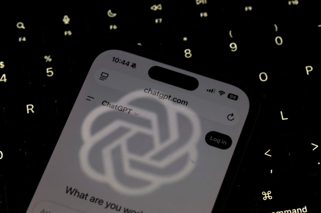 A smartphone displaying the ChatGPT website, illuminated against a dark keyboard background.