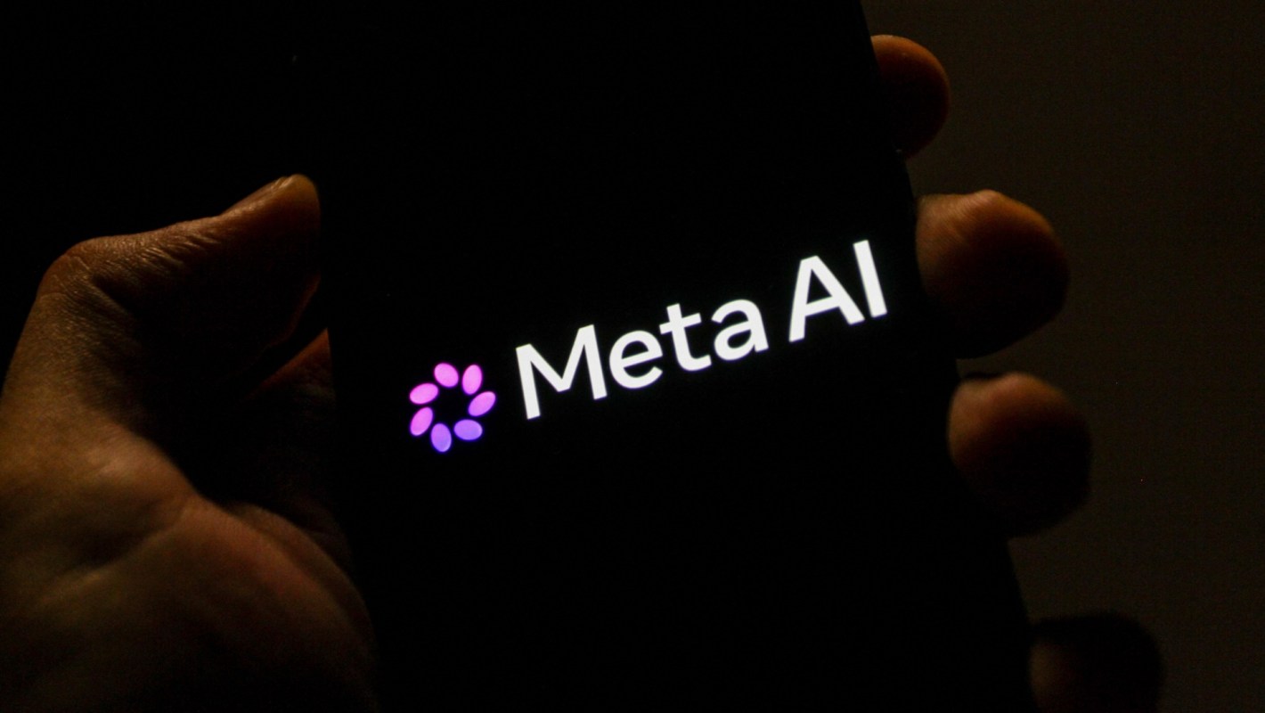 A hand holds a smartphone displaying the logo of Meta AI in a dimly lit environment.