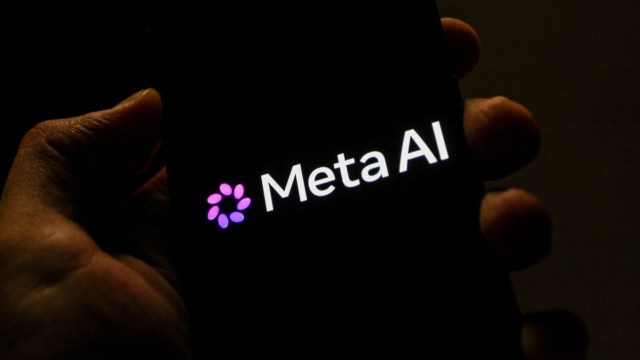 A hand holds a smartphone displaying the logo of Meta AI in a dimly lit environment.