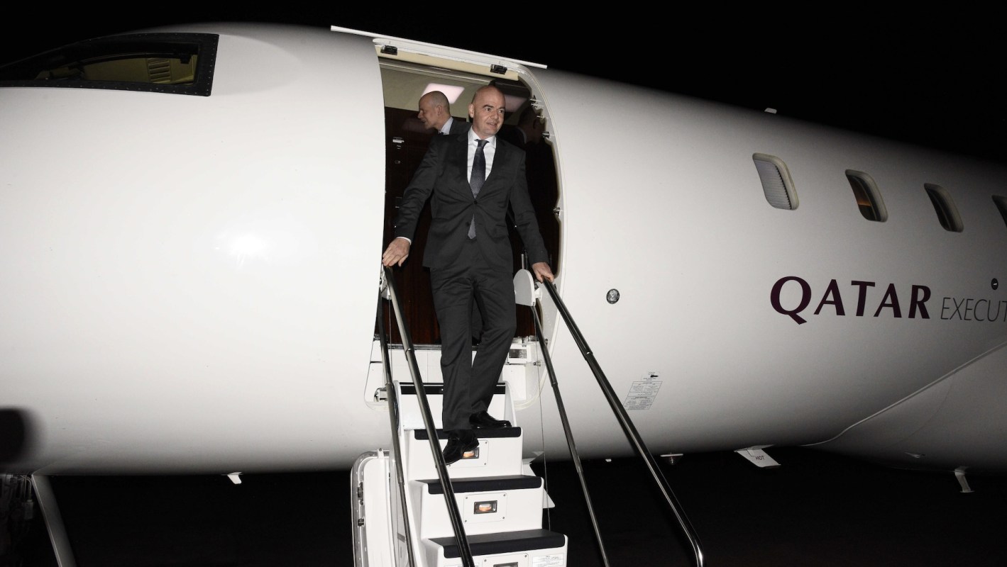A man in a suit descends the steps of a private jet at night, with the Qatar Executive logo visible.