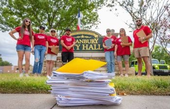 Residents looking at a stack of papers on the ground while standing in front of a Granbury city hall sign.