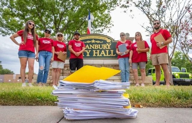 Residents looking at a stack of papers on the ground while standing in front of a Granbury city hall sign.