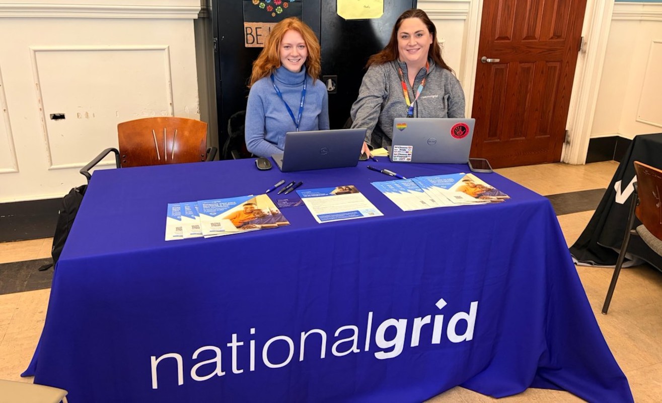 Two women seated at a table covered with a blue cloth displaying "national grid," surrounded by informational materials.