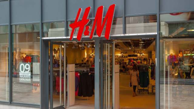An H&M clothing store entrance featuring a large red logo and displays of apparel inside.