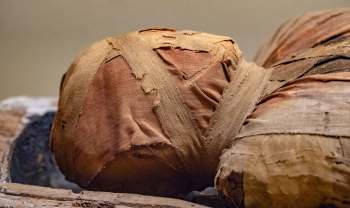 A close-up of an ancient mummified object wrapped in faded fabric and bandages.