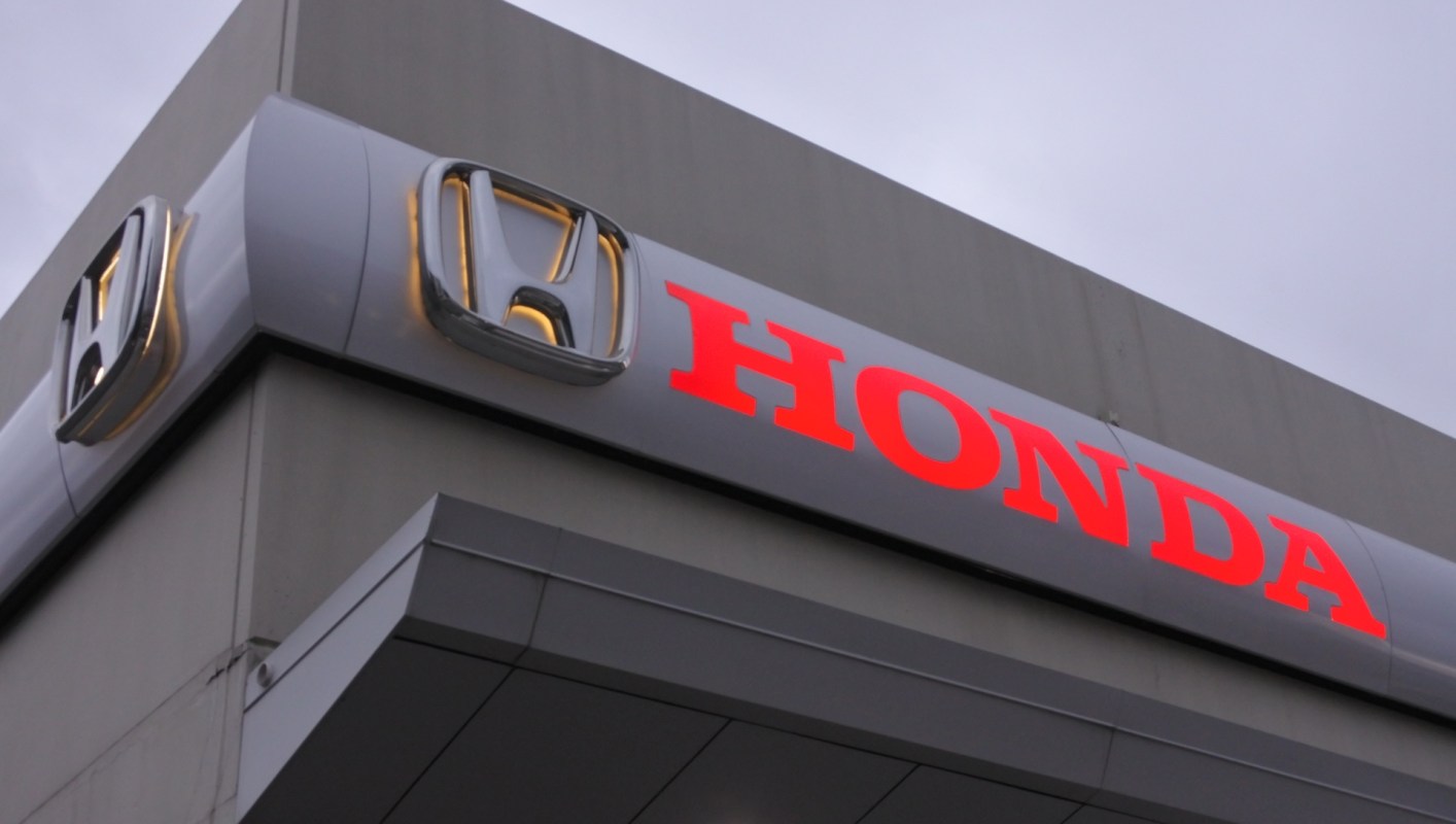 A close-up view of a dealership sign displaying the Honda logo in illuminated letters.