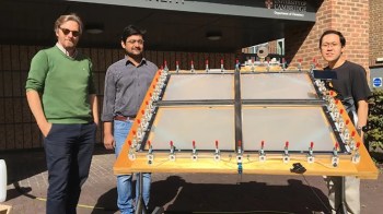 Three researchers stand beside a large experimental setup.
