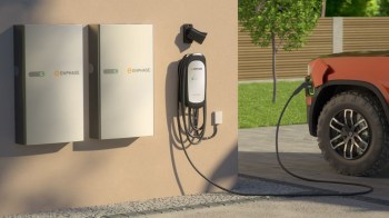 An electric vehicle is charging at a wall-mounted charger next to two energy storage units.
