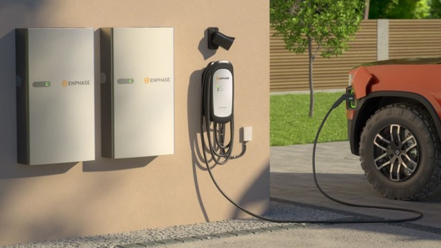An electric vehicle is charging at a wall-mounted charger next to two energy storage units.