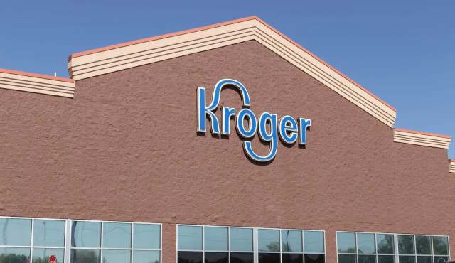A storefront of a Kroger grocery store with large blue lettering on a brown exterior wall.