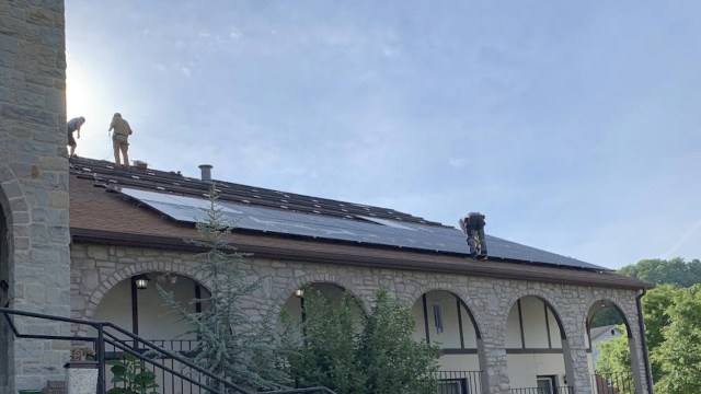 Workers installing solar panels on the sloped roof of a stone building.