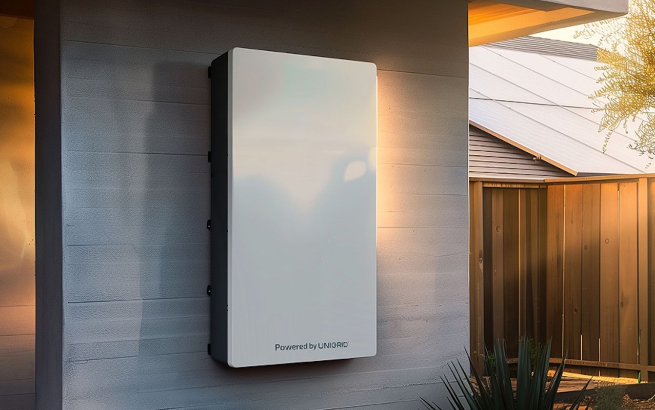 A white energy storage unit mounted on a wall in a residential outdoor setting.