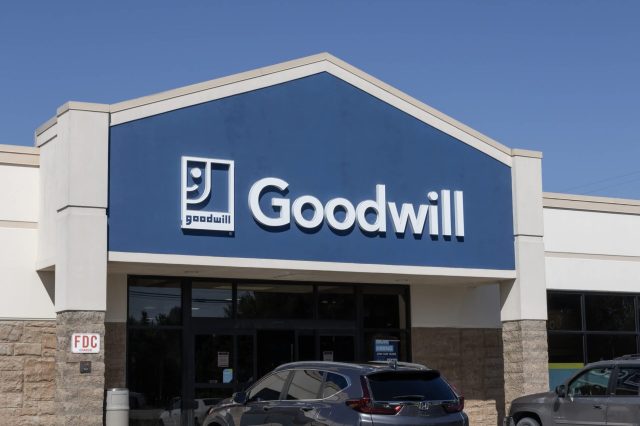 A Goodwill store front with a blue sign and a "Now Hiring" notice on the window.