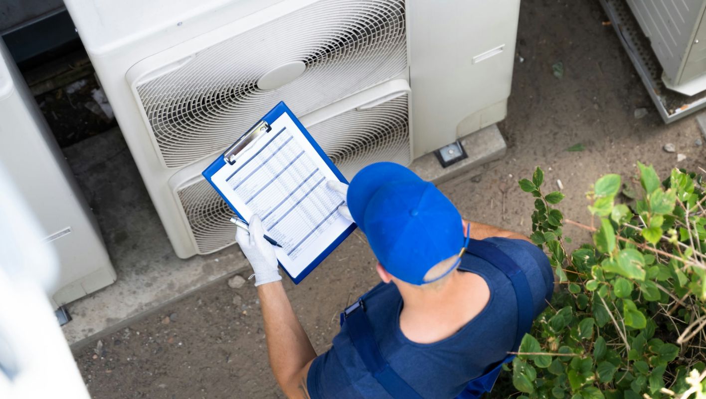 A technician wearing gloves examines a clipboard near outdoor air conditioning units.