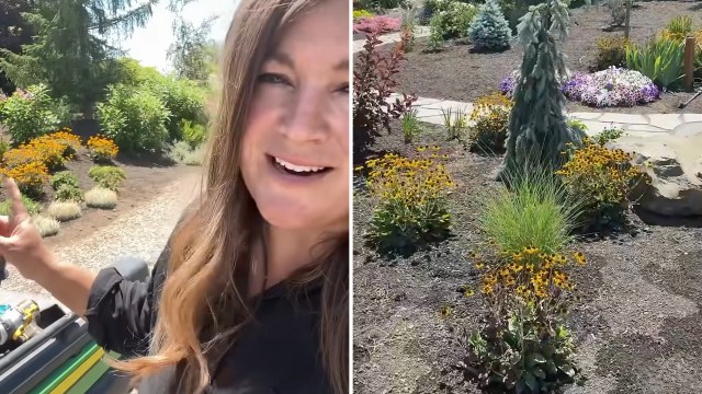 A woman gestures while standing in a vibrant garden filled with flowers and lush greenery on a sunny day.