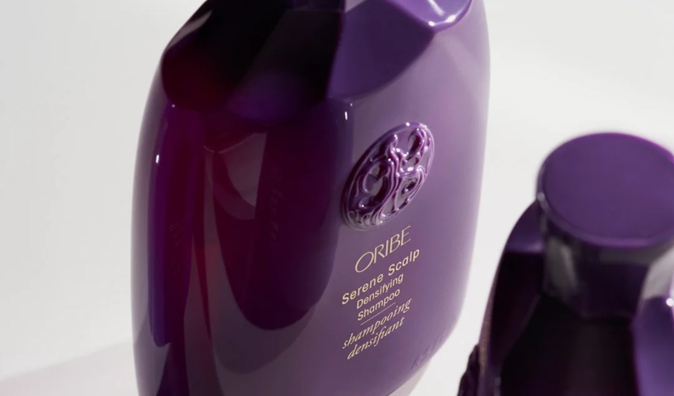 A close-up of Oribe Serene Scalp Densifying Shampoo bottle in rich purple with an ornate logo.