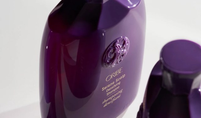 A close-up of Oribe Serene Scalp Densifying Shampoo bottle in rich purple with an ornate logo.