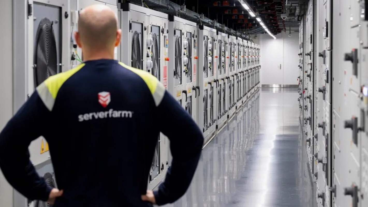 A technician observing cooling units in a modern server room with rows of equipment.