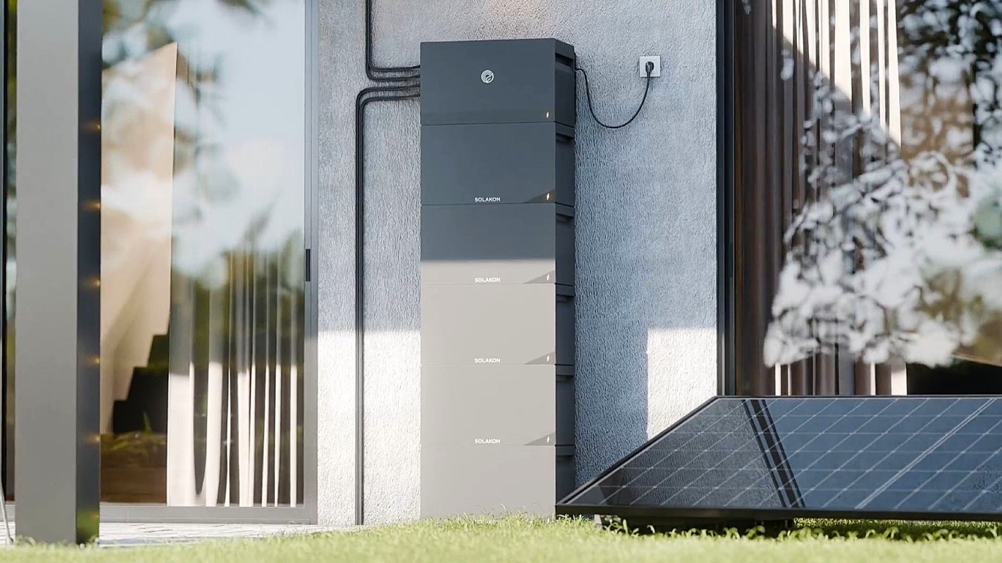 A vertical battery storage unit next to a solar panel and modern building exterior.
