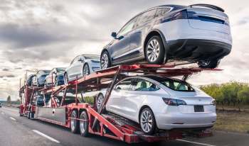 A car carrier truck transporting multiple Tesla vehicles on a highway under a cloudy sky.