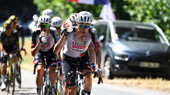 A group of cyclists in a race, with one rider spraying water while others drink from bottles.