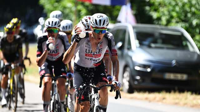 A group of cyclists in a race, with one rider spraying water while others drink from bottles.