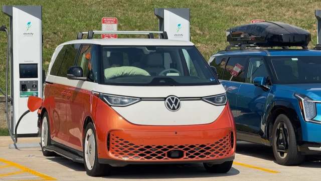 A Volkswagen electric vehicle with an orange and white design is charging at an electric station alongside another car.