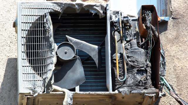 A damaged air conditioning unit with charred components, wires exposed, and a missing protective cover.