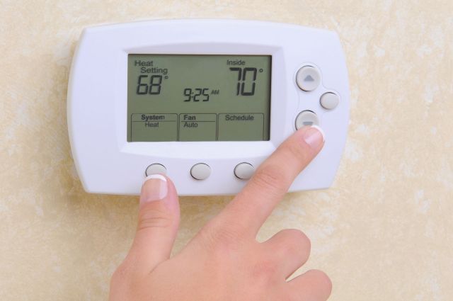 A hand adjusts a digital thermostat displaying a room temperature of 70°F.