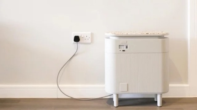 A white home battery storage unit plugged into a wall socket on a light-colored wall.