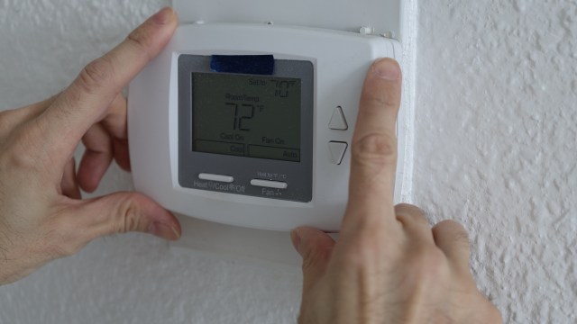 A person adjusting a digital thermostat displaying a setting of 72°F.