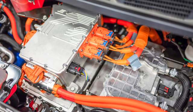 An electric vehicle's power electronics assembly with orange wiring and connectors visible on a metal chassis.