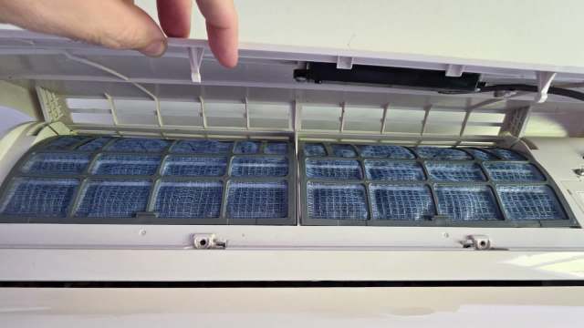 A person holds open the cover of an air conditioning unit, revealing its blue mesh filters.
