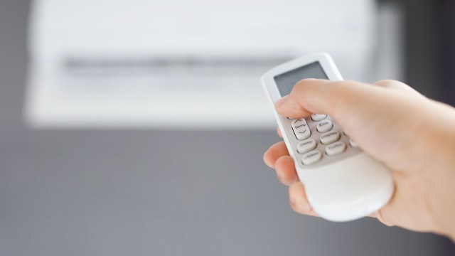 A person using a remote control to adjust HVAC settings.