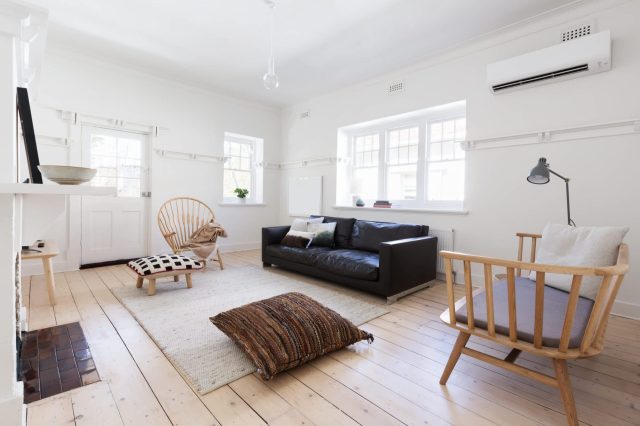 A bright living room featuring a black couch, wooden armchair, and natural wood flooring with soft furnishings.