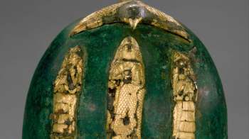A decorative green egg adorned with gold figures and a bird on top, showcasing ancient craftsmanship.