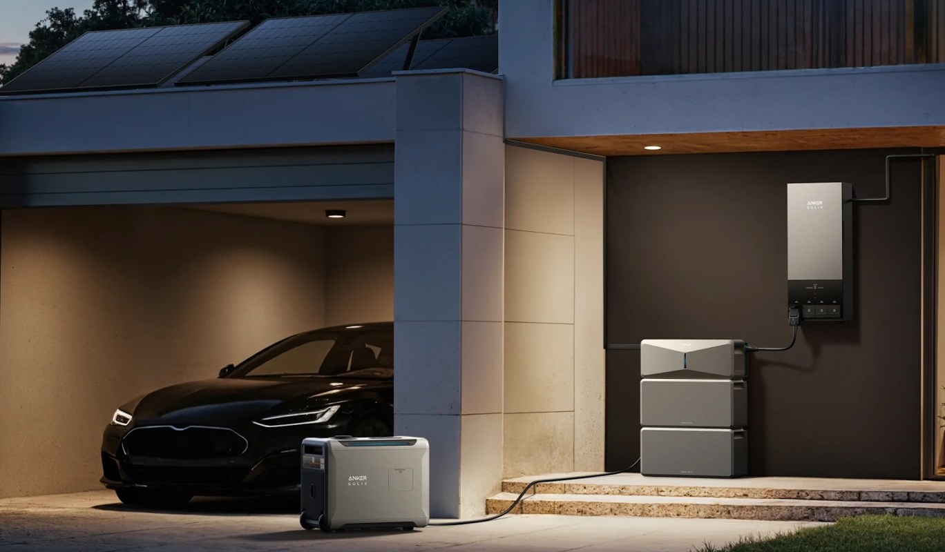 A sleek black electric vehicle parked in a garage with solar panels, a power station, and battery storage setup.