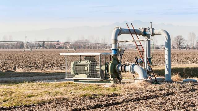 A water pump system with pipes is installed on a dry agricultural field under a clear sky.