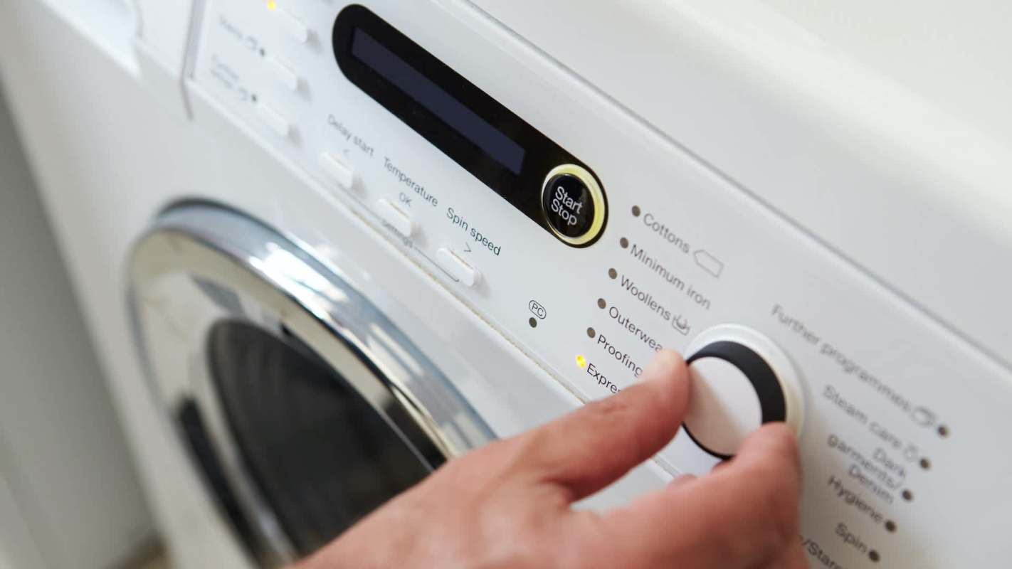A close-up of a person's hand adjusting the settings on a washing machine's control panel.