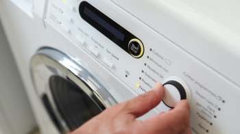 A close-up of a person's hand adjusting the settings on a washing machine's control panel.