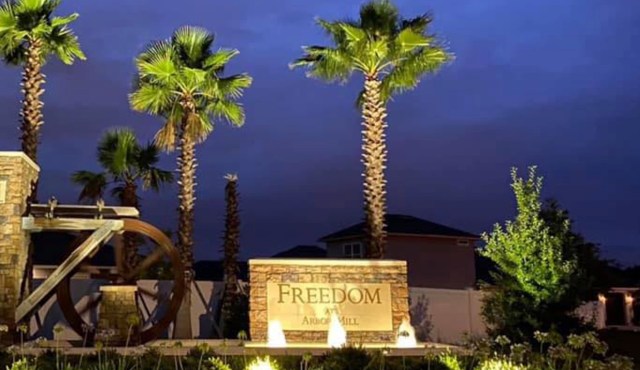 A stone sign reading "Freedom at Arbor Mill" illuminated at night, surrounded by palm trees and landscaping.