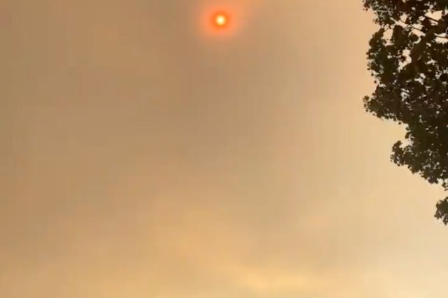 A smoky sky with a faint red sun peeking through, partially obscured by haze.